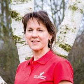 Porträt einer Frau vor einem Birkenwald. Sie lächelt in die Kamera.