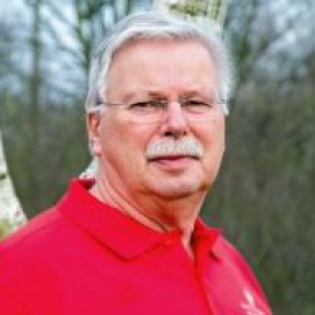 Porträt eines Mannes in rotem Poloshirt vor einem Hintergrund aus Bäumen
